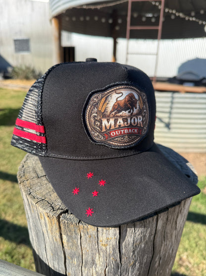 A black Major Outback trucker hat with a red and black striped side stripe and a large embroidered front patch, displayed on a weathered wooden post outdoors.